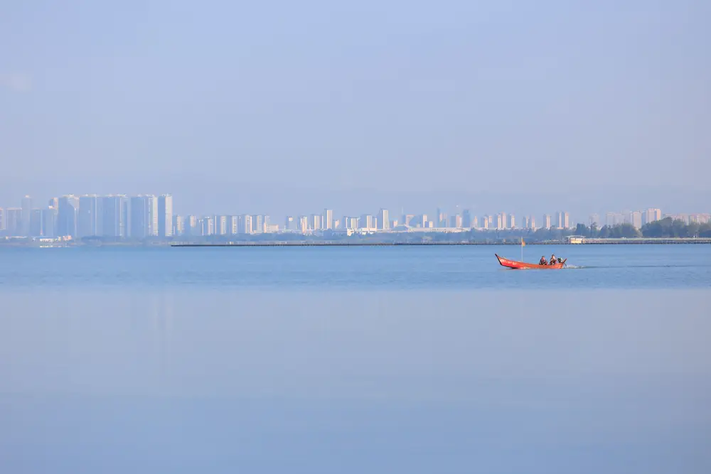 平静湖面红色小船 远景雾色城市天际线