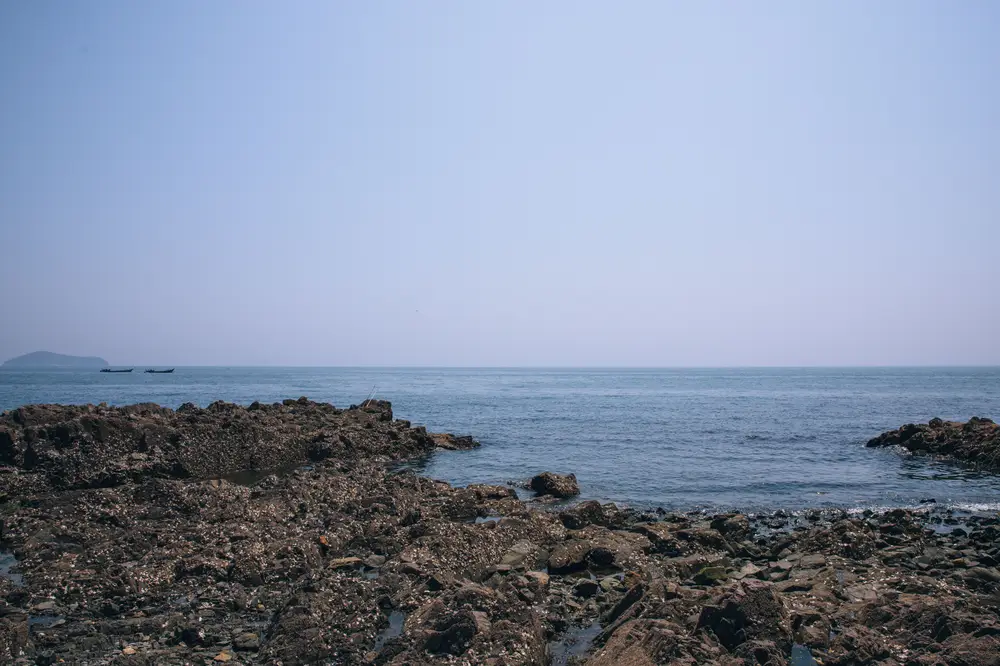 海滨礁石滩远景海面晴空与远岛渔船
