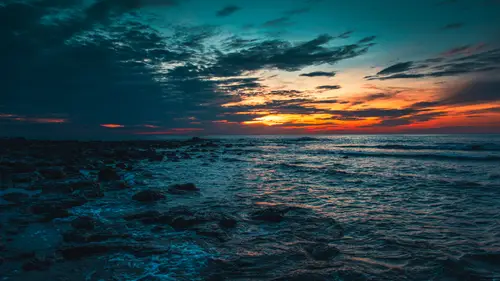 6594x3709 Desktop Wallpaper - 日落时分岩滩海岸 橙红晚霞与青蓝色海面形成强烈色彩对比